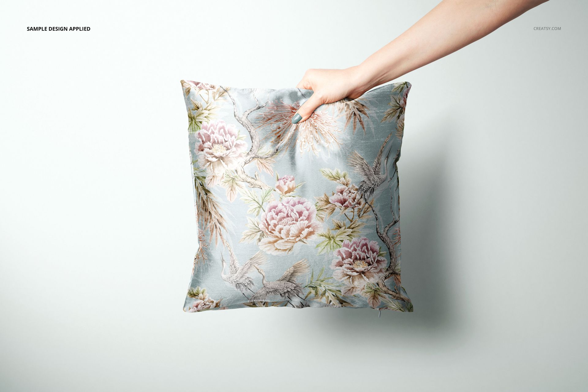 PSD mockup showing a square pillow cover with soft botanical motif, displayed in a minimal indoor setting.