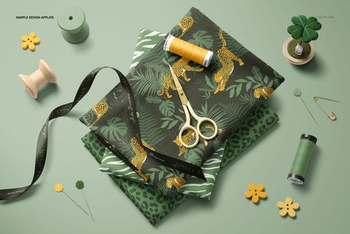 Jersey fabric mockup featuring stacked patterned textiles and various sewing tools on a light green background.