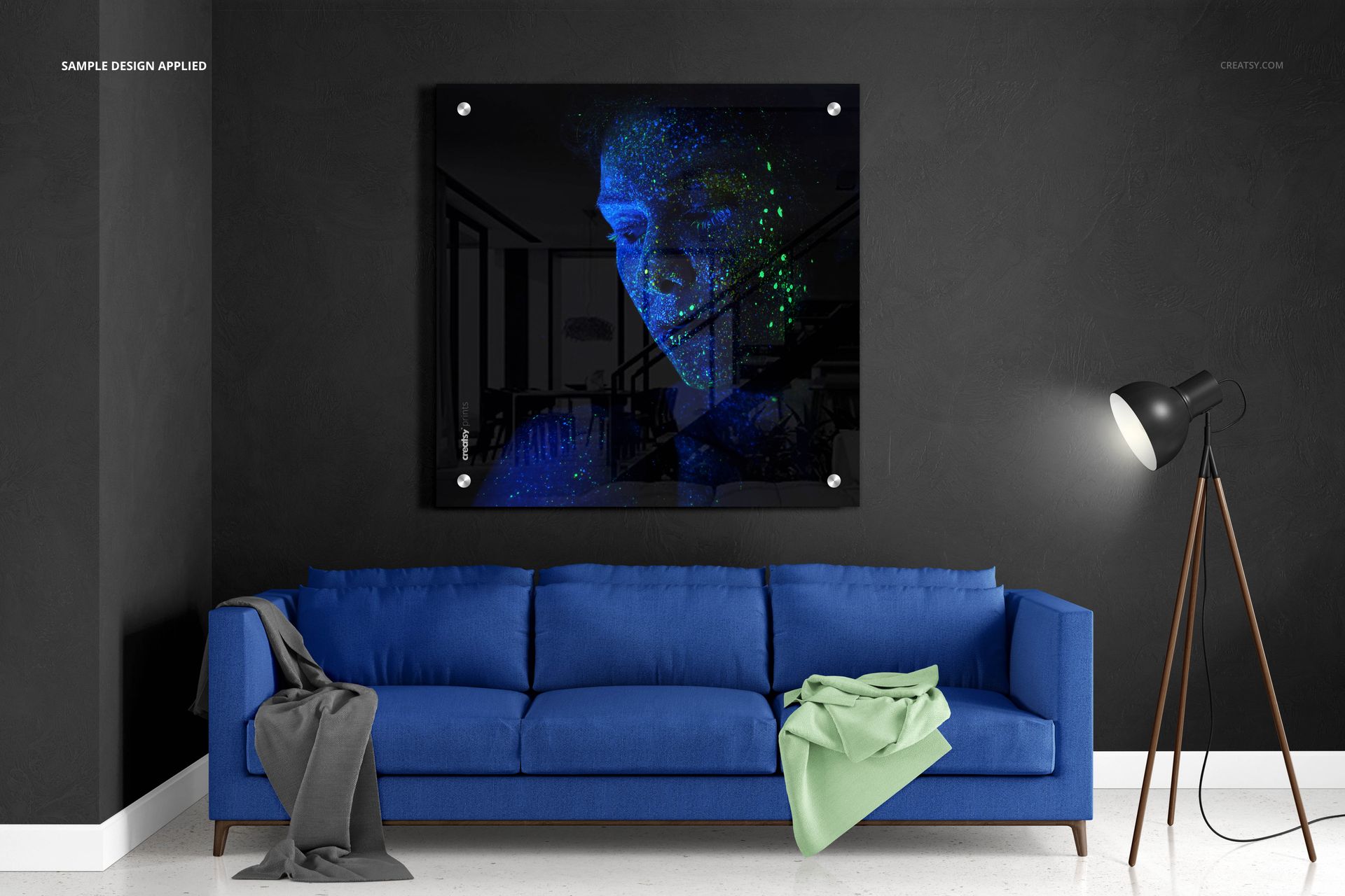 Square acrylic print mockup displayed above a blue sofa in a modern living room with dark walls and a floor lamp.