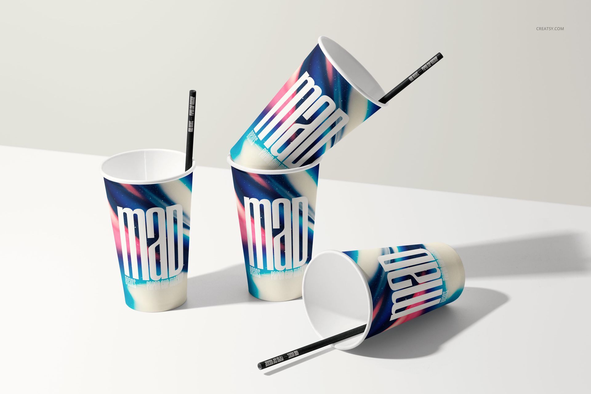 PSD mockup of paper cups with graphic prints and black straws, displayed on a clean white tabletop in bright lighting.