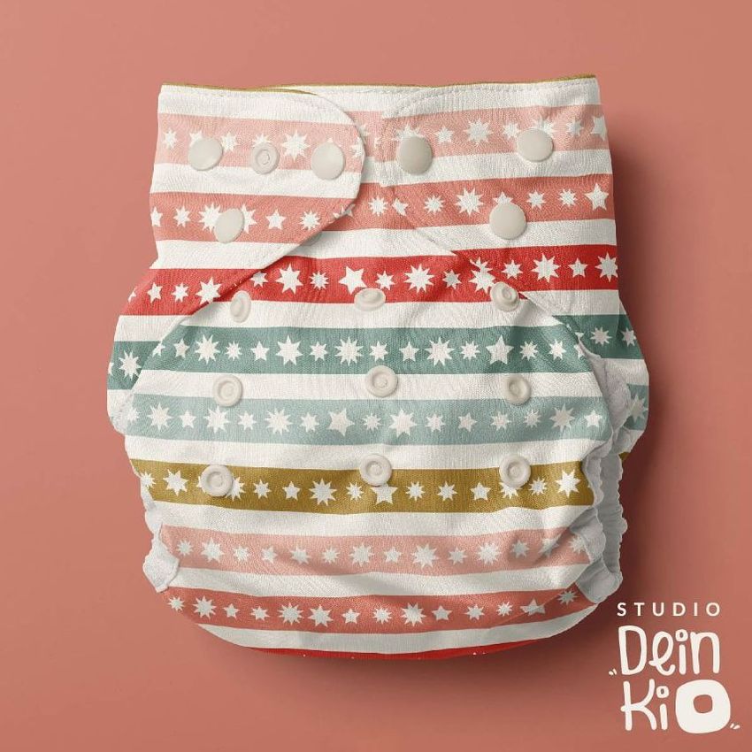 Reusable baby cloth diaper mockup featuring horizontal stripes in pastel pink, green, and gold with star patterns on a muted pink background.