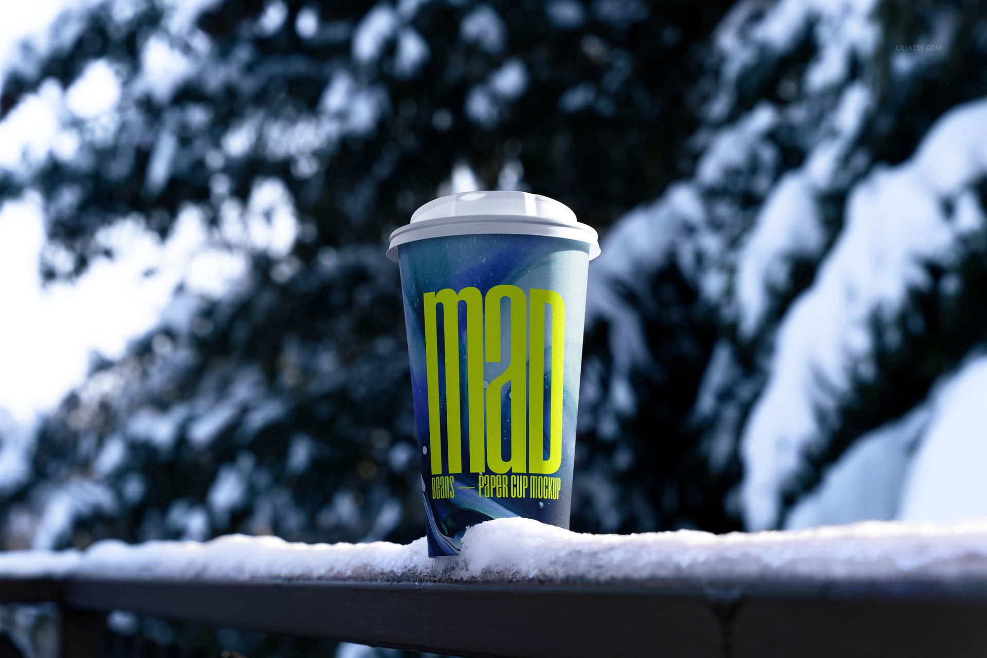 Winter-themed paper cup mockup with a blue and yellow design, white lid, and snow-covered scenery in the background.