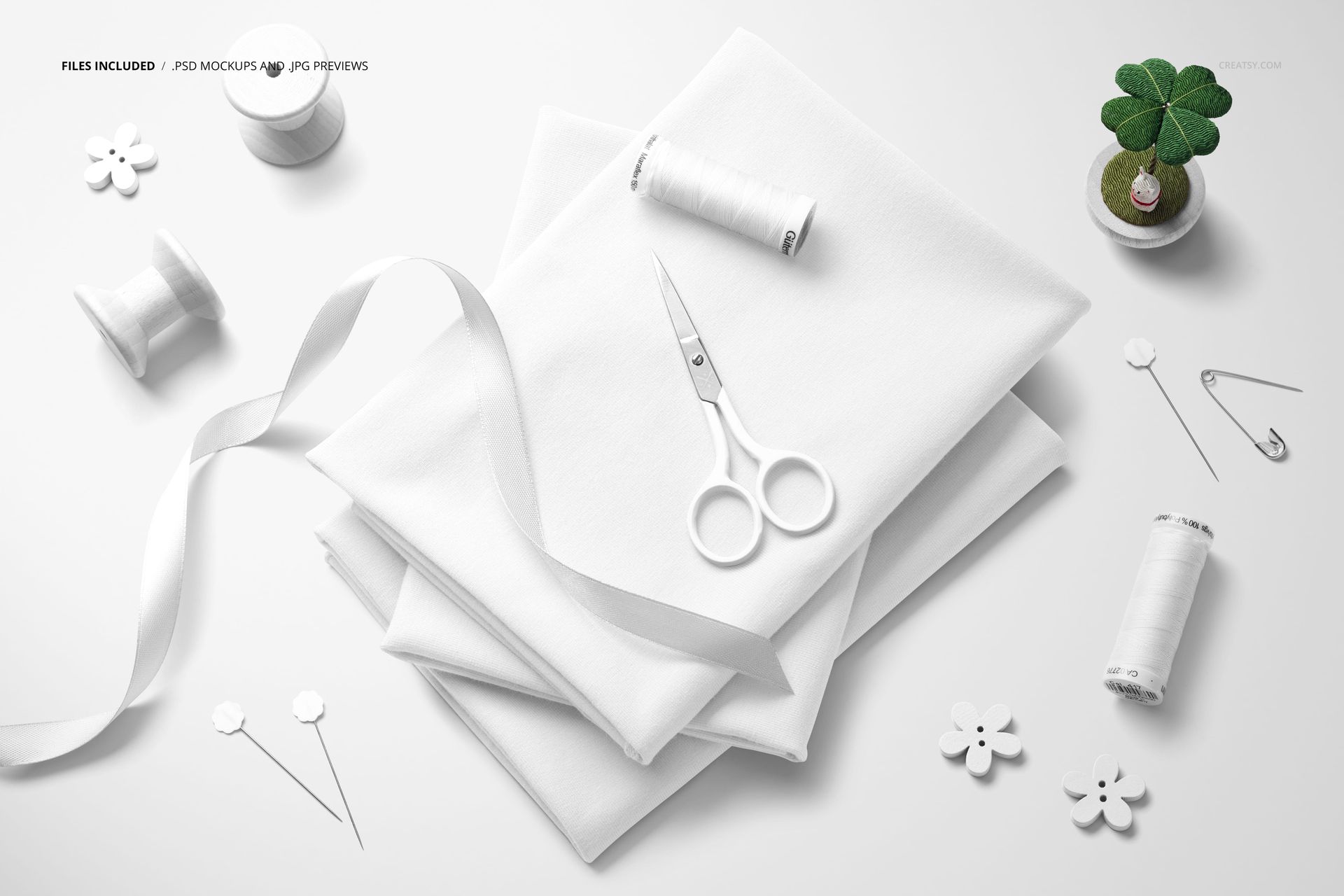 PSD mockup showing folded jersey fabric, white ribbon, sewing scissors, thread spools, and small floral decorations.