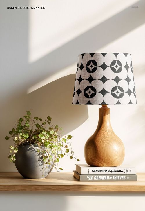 PSD mockup of a wood table lamp with a black and white circular patterned shade, placed on books and a shelf.