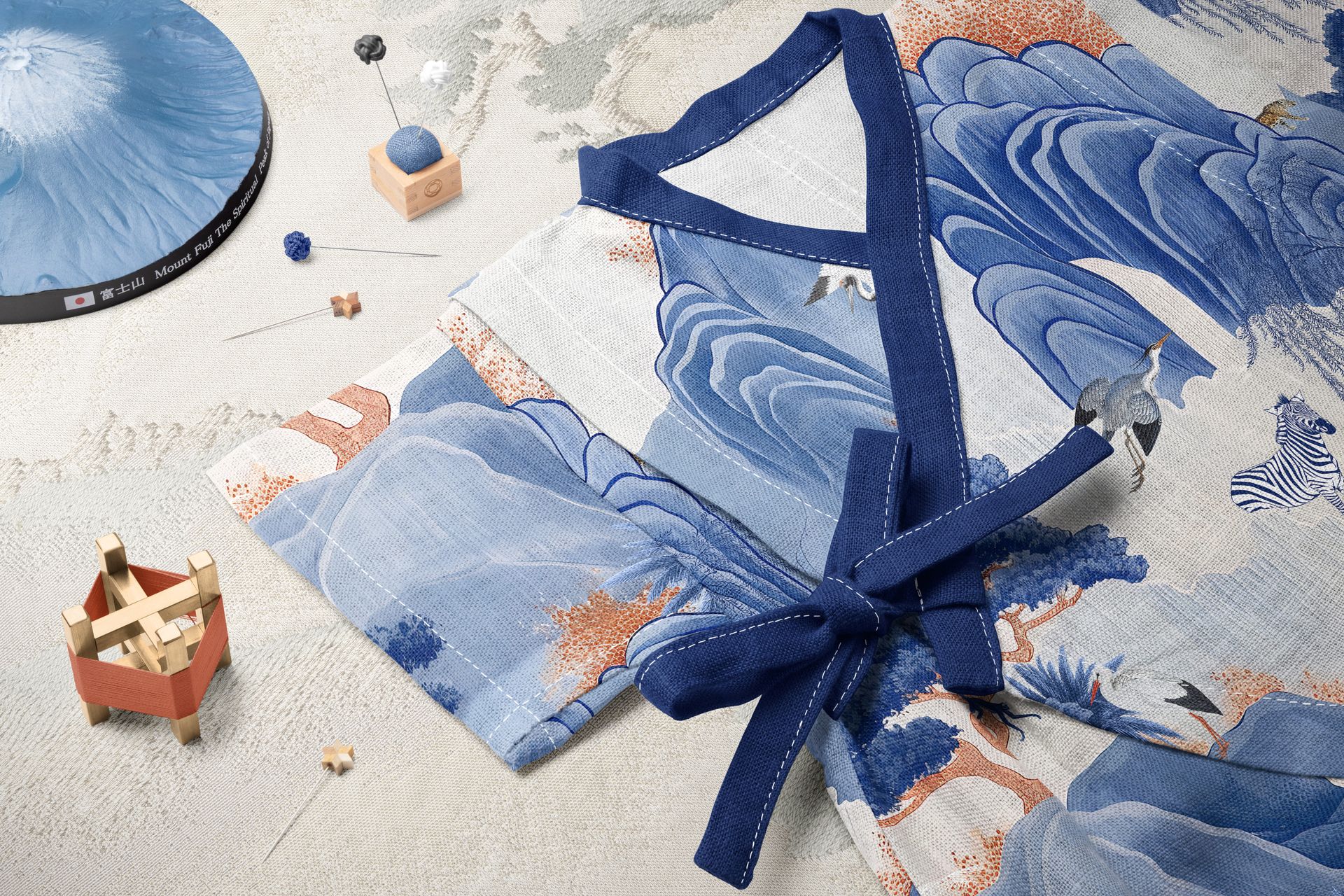 Baby romper mockup with traditional Japanese landscape print, styled with a temari ball, needle pad, and wooden blocks.