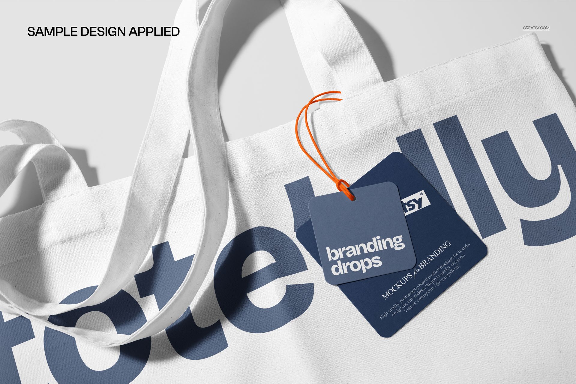 Canvas tote bag mockup featuring a close-up of white fabric handles and a blue tag with orange string detail.