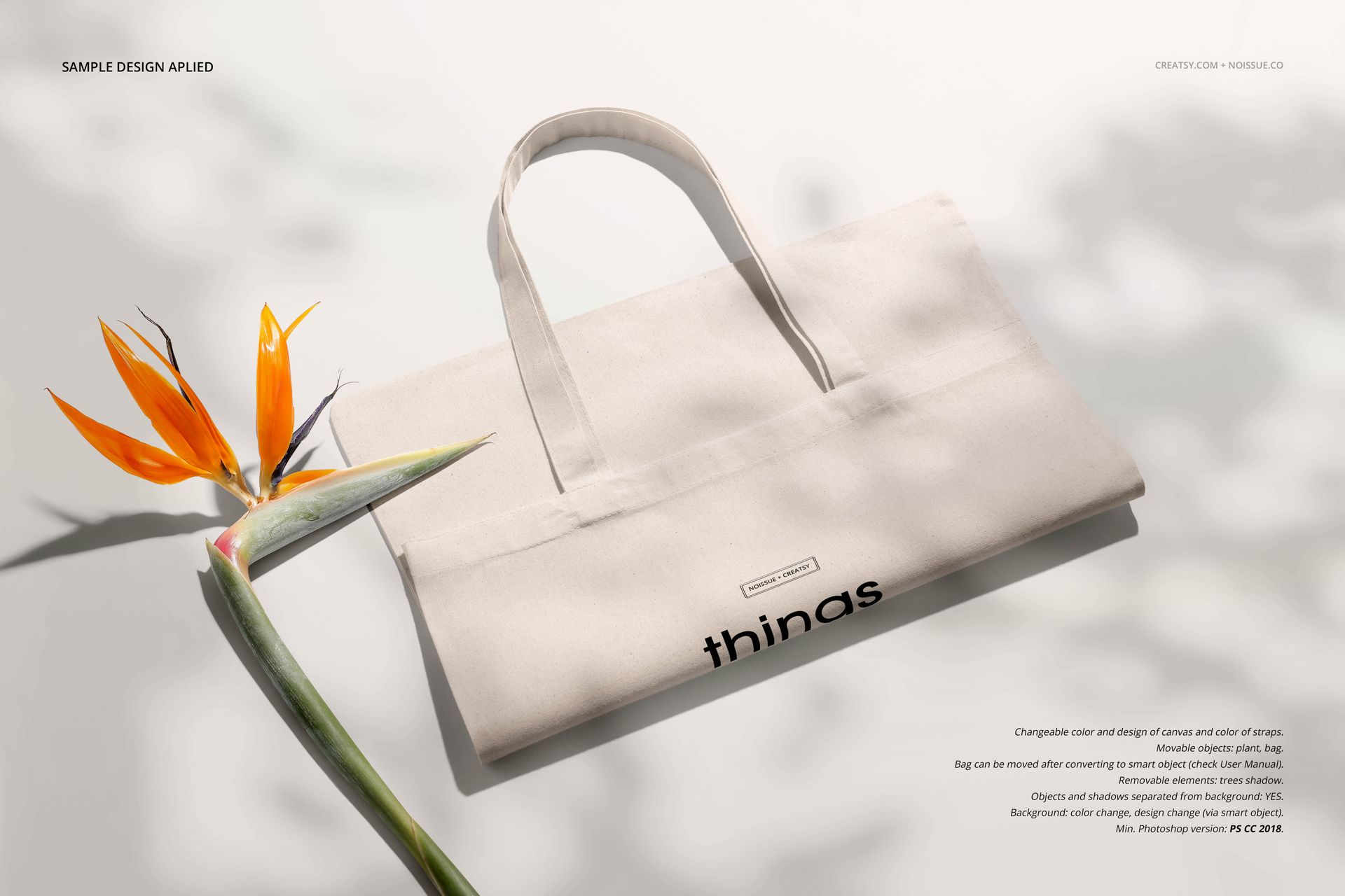 Neutral-colored tote bag mockup displayed on a light surface with a bird of paradise flower, front view.