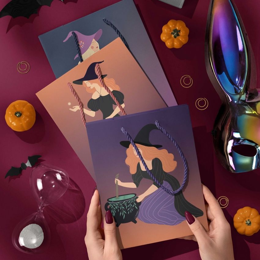 Halloween paper gift bag mockup featuring illustrated witches on purple and orange backgrounds, surrounded by pumpkins and props.