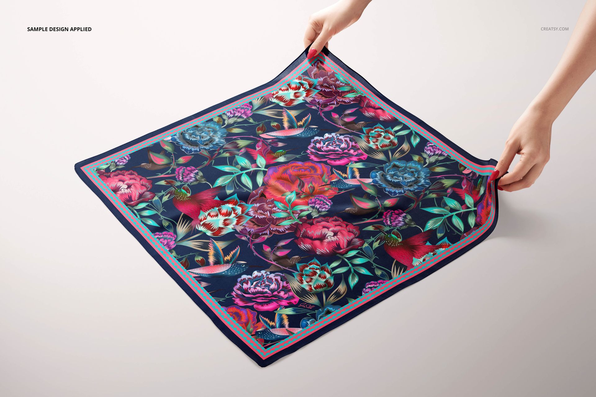 Colorful square silk scarf mockup featuring bold flowers and birds, viewed from above with hands at edges.