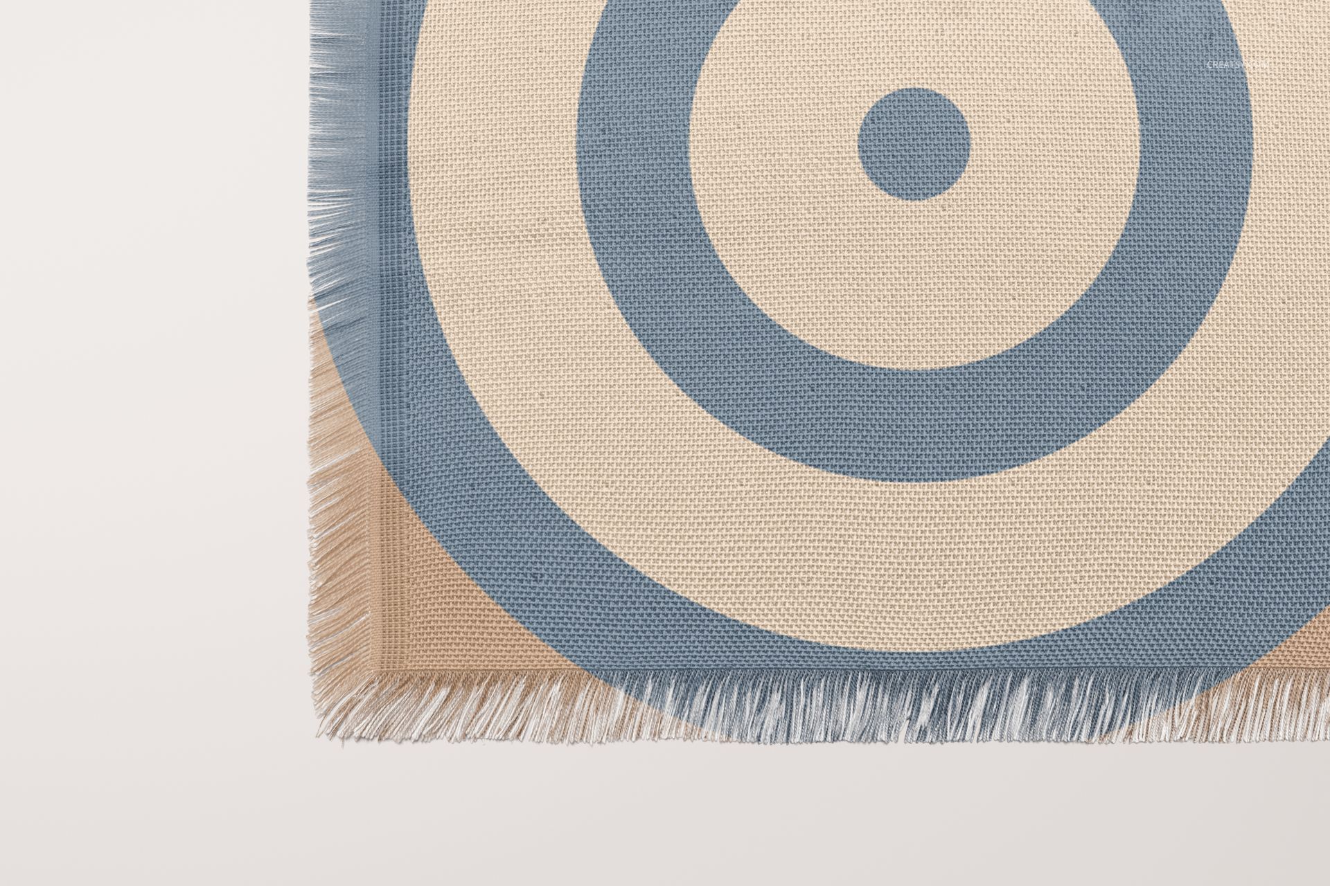 Front view of a woven coverlet mockup featuring blue circular design and textured fabric with visible fringe.