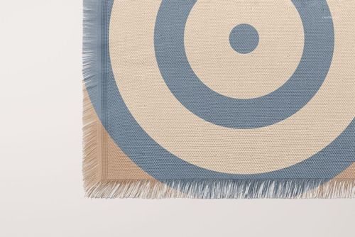 Front view of a woven coverlet mockup featuring blue circular design and textured fabric with visible fringe.