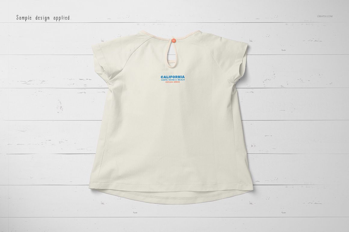 Back view of a short-sleeve baby t-shirt mockup in light cream color, displayed on a white wooden surface.
