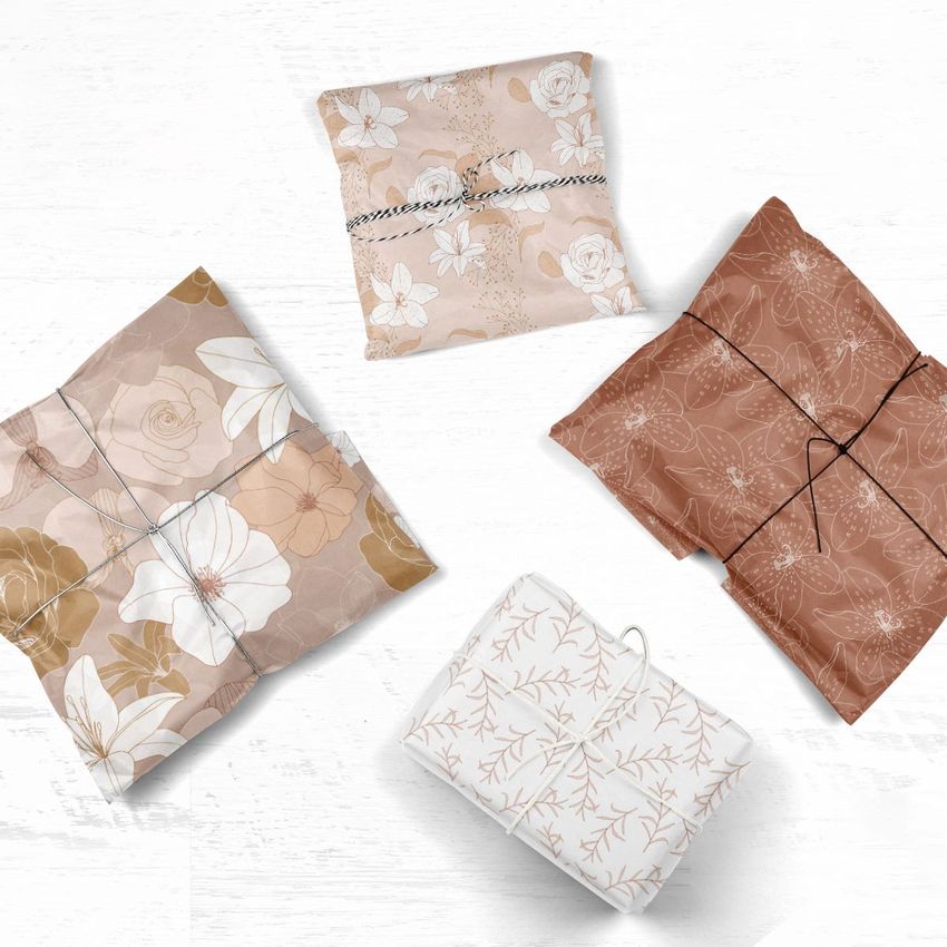 Four gift packages wrapped in patterned tissue paper are arranged on a white wooden surface, each tied with thin string.
