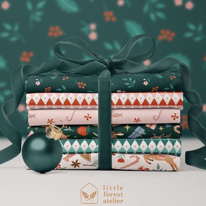 Fabric stack mockup featuring folded Christmas-themed textiles tied with a dark green ribbon, set beside a green bauble.