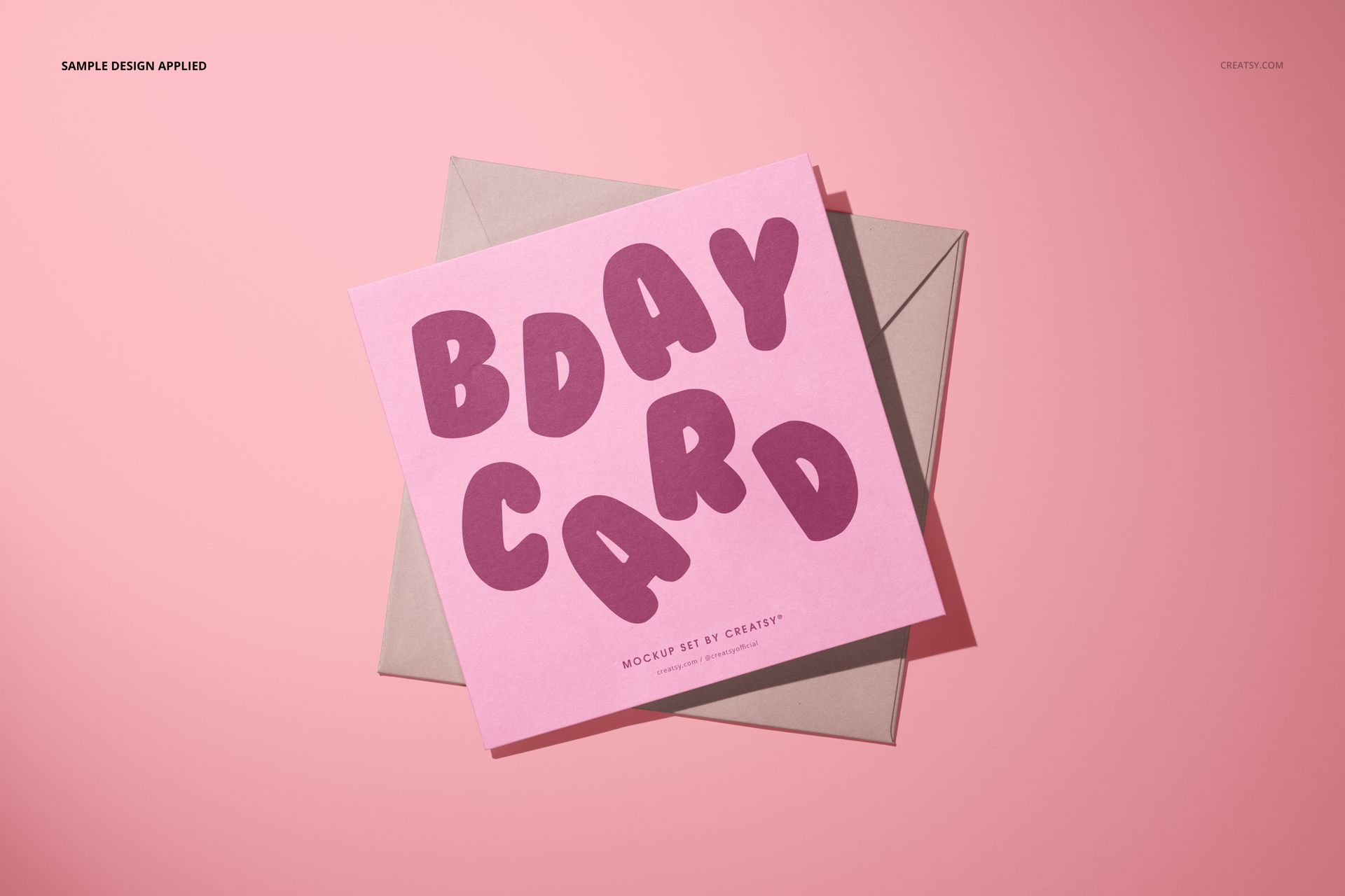Greeting card PSD mockup showing a pink card with playful purple text, positioned over a beige envelope, top view.