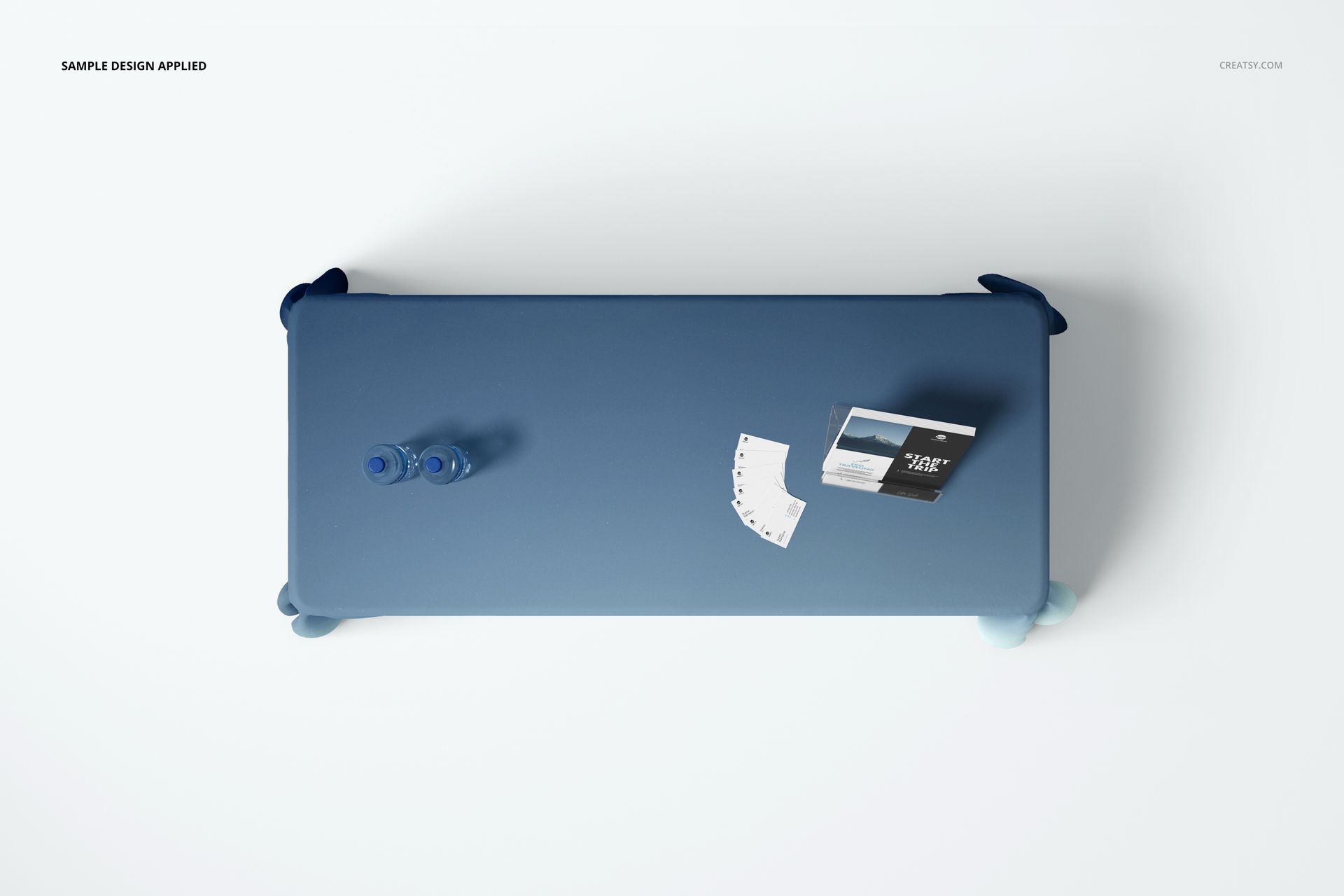 PSD mockup showing a blue polyester tablecloth from above, with water bottles and printed cards on a white background.