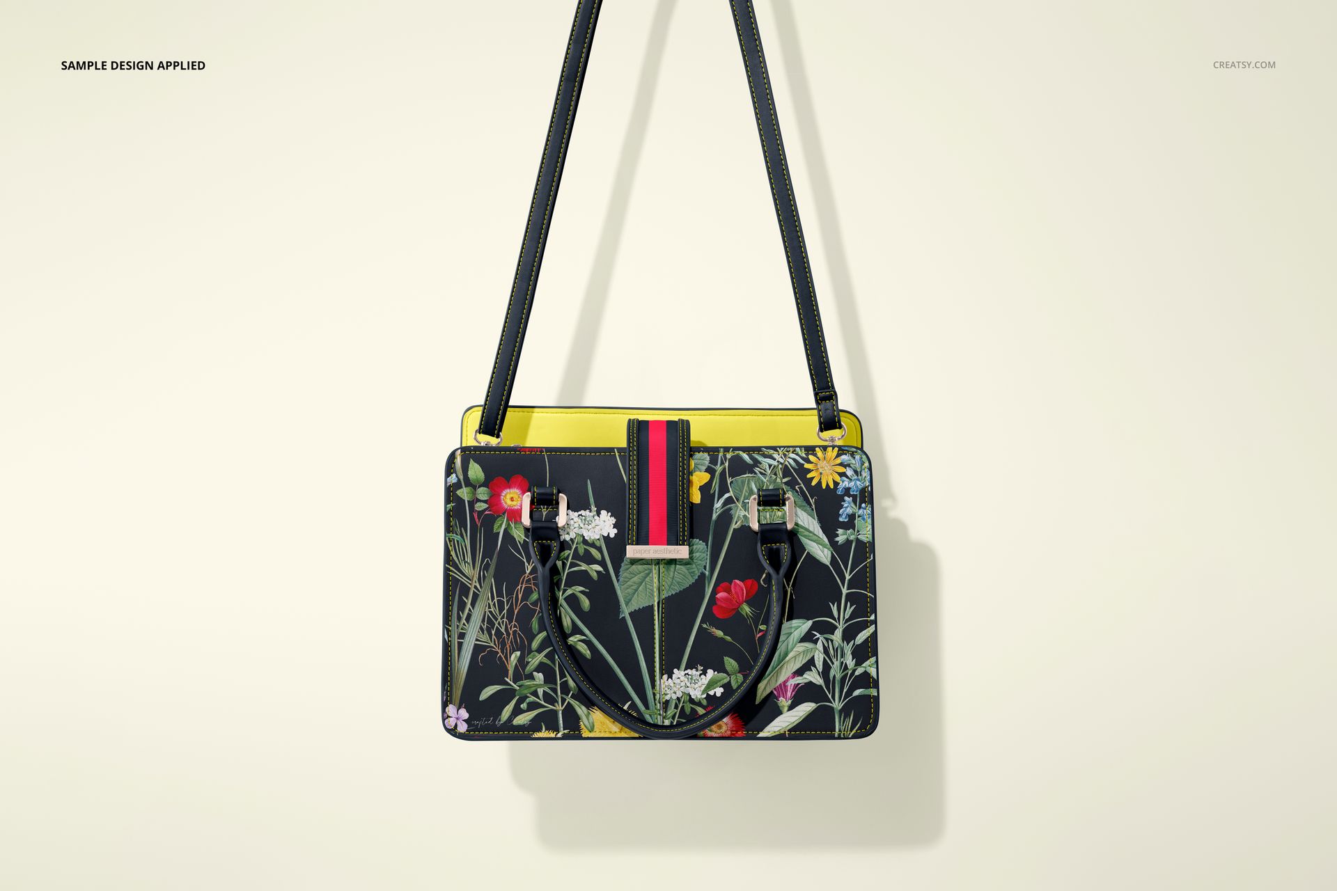 Leather handbag mockup featuring a botanical print, black straps, and yellow trim, displayed on a neutral background.