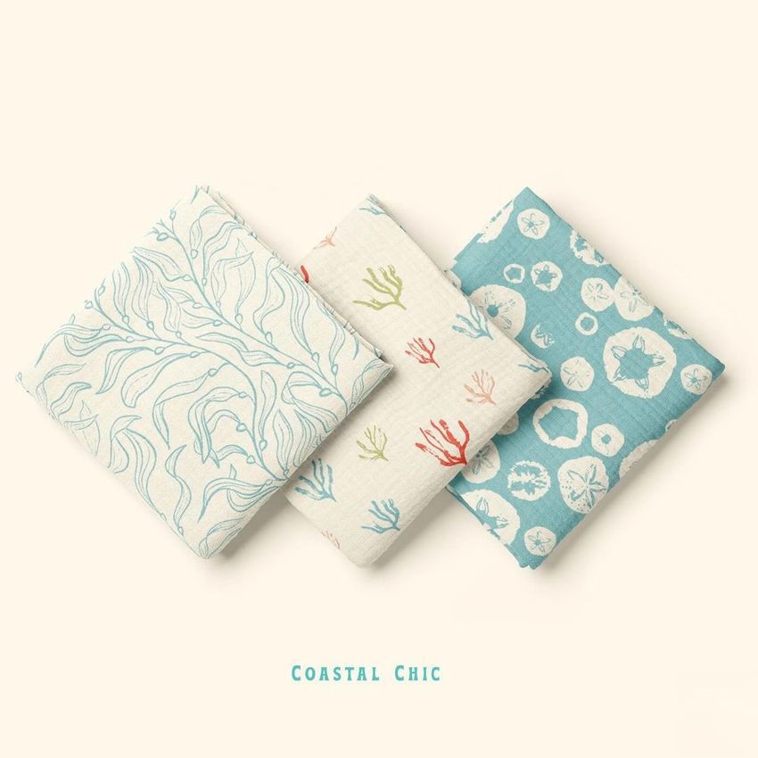 Three crinkle muslin swaddle blankets are folded and arranged side by side on a light background, each with a different coastal-inspired pattern.