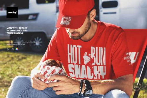 PSD mockup showing a person seated by a food truck, grasping a burger with branded wrapping and wearing red apparel.