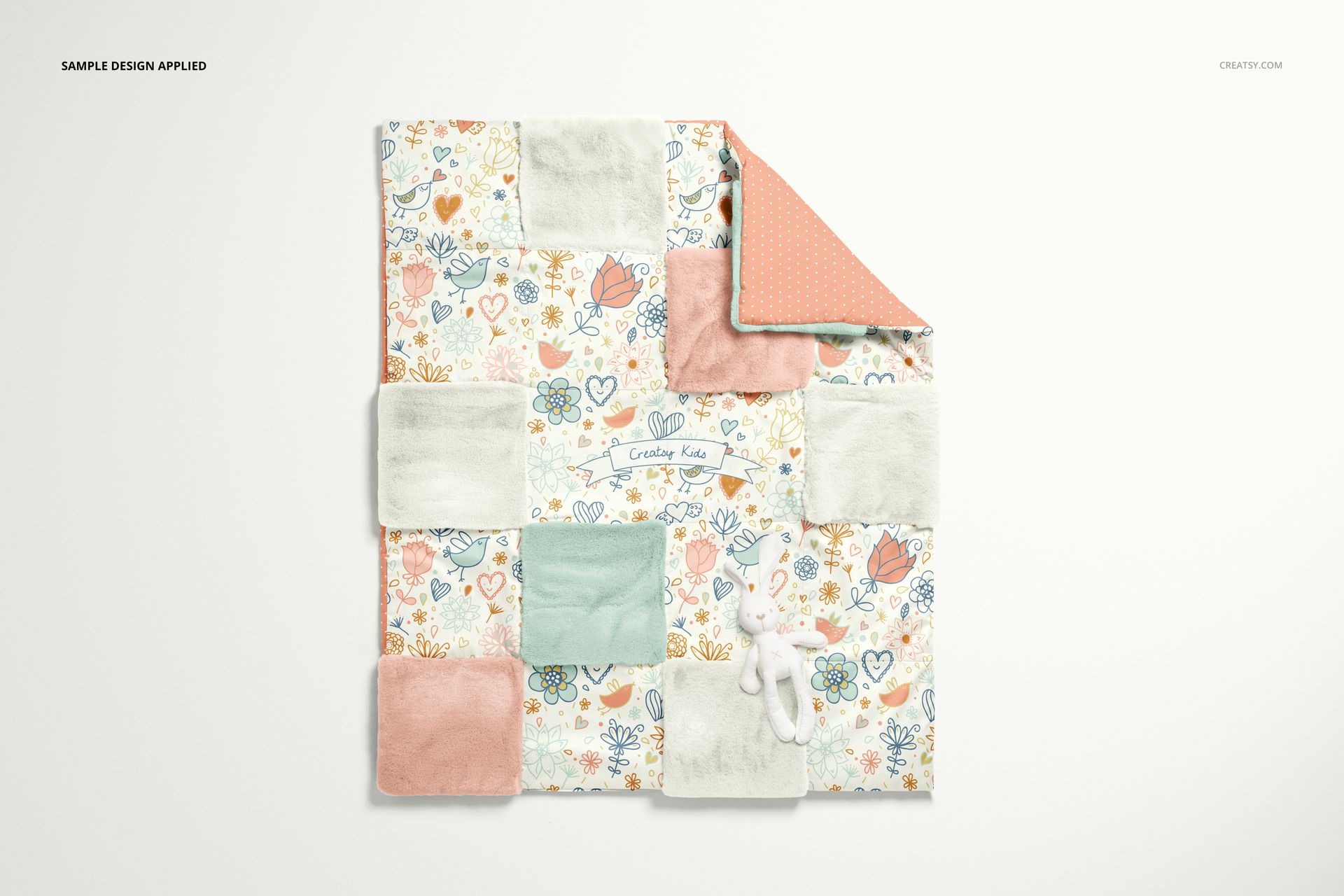Top view of a baby patchwork quilt mockup featuring soft fleece squares, floral motifs, and a small plush toy.