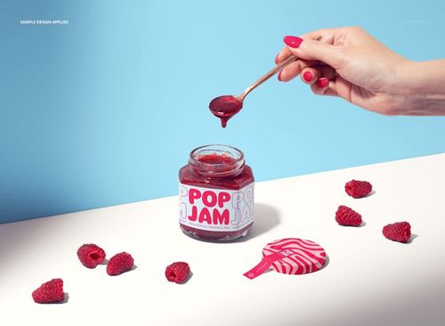 Raspberry jam jar mockup on a white surface with loose raspberries, spoon, and bright blue background.
