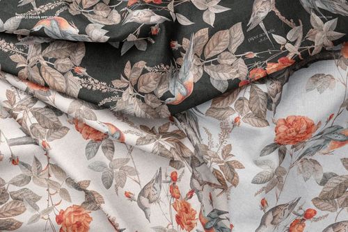 Creased fabric mockup featuring two pieces of cloth with floral and bird patterns in muted orange and gray tones.