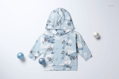 Mockup of a baby velour tracksuit top in pastel blue with aviation print, laid out on a white surface with decorative balls.