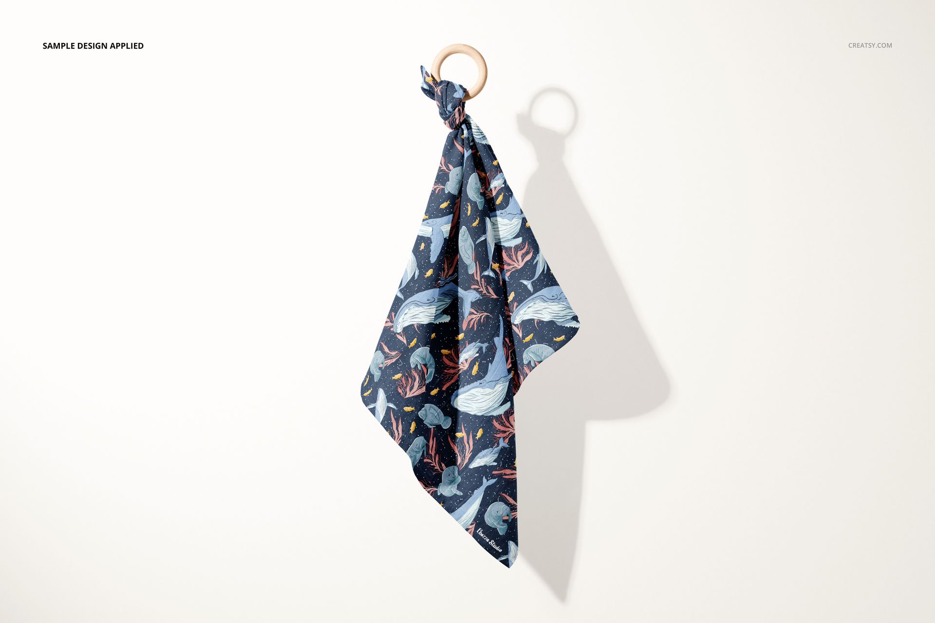 Muslin cloth wooden teether mockup showing a patterned dark blue fabric tied to a round wooden ring, front view on a light background.