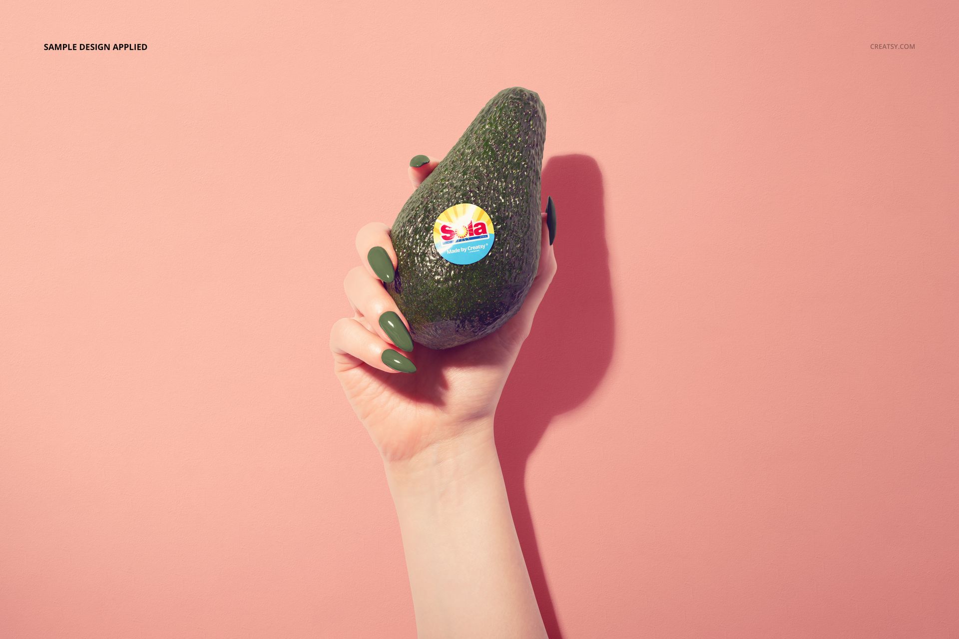 Avocado fruit mockup showing a sticker on the peel, held by a hand, with a minimalist pink background.
