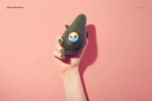 Avocado fruit mockup showing a sticker on the peel, held by a hand, with a minimalist pink background.