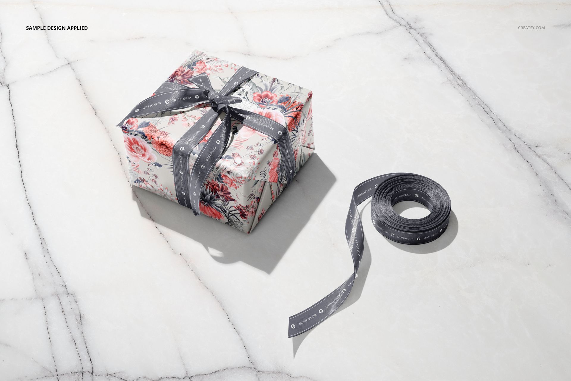 Gift box mockup featuring floral wrapping paper and a gray ribbon, displayed on a light marble background.