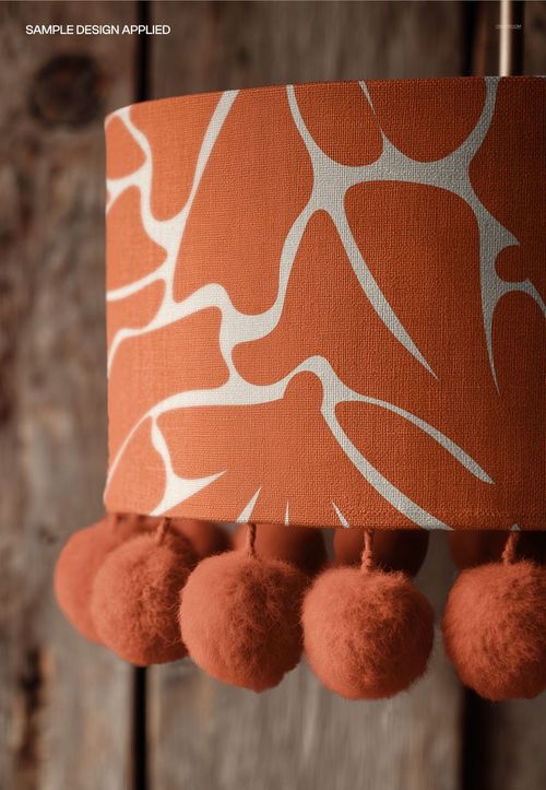 Detailed view of a lampshade mockup featuring a bold orange design with white lines and fluffy pom pom trim.