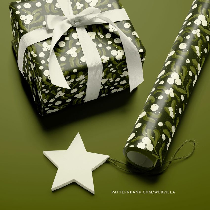 Gift wrapping paper mockup featuring a wrapped box with white ribbon, a matching roll, and a white star ornament on a green surface.