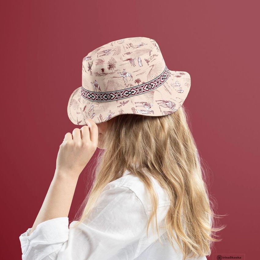 A woman wearing a reversible bucket hat mockup with a desert-themed pattern and geometric band, shown from behind against a red background.