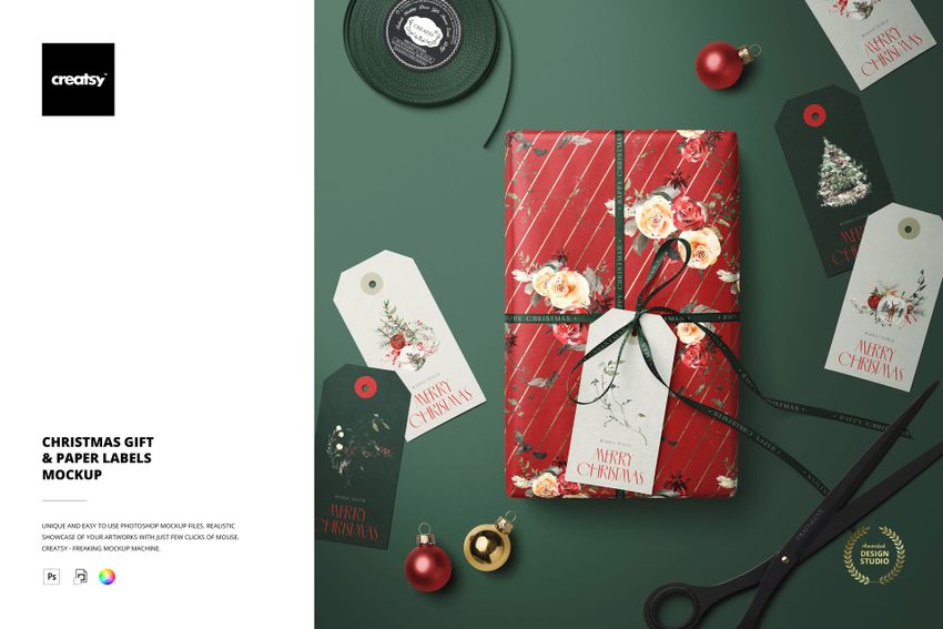 Christmas gift mockup featuring a wrapped present with ribbon, paper labels, scissors, and holiday decorations on a green surface.