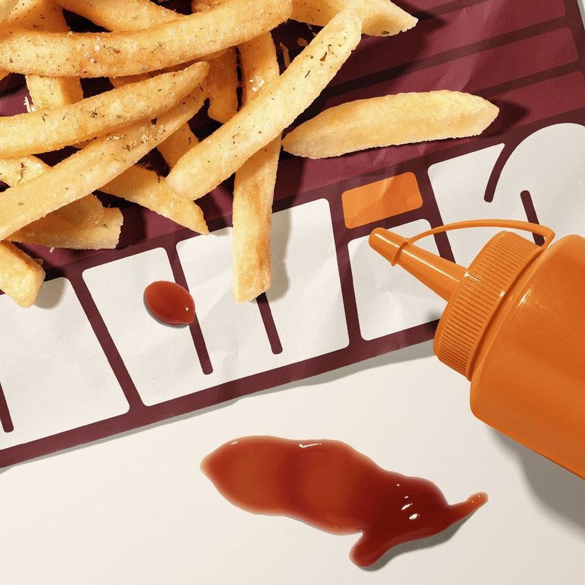 Food safe paper mockup featuring seasoned french fries on a patterned sheet with a squeeze bottle and spilled ketchup in the foreground.