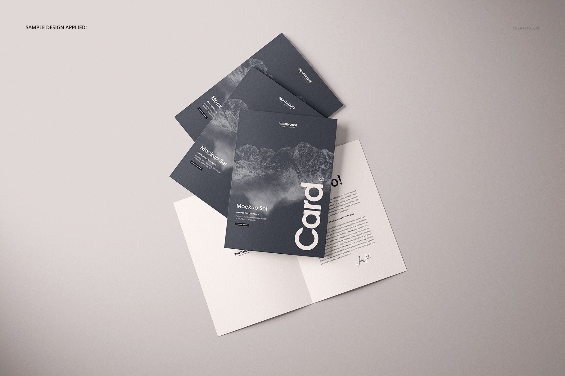 Folded A4 cards mockup set displayed on a light surface, featuring dark covers with mountain graphics and an open card showing text.