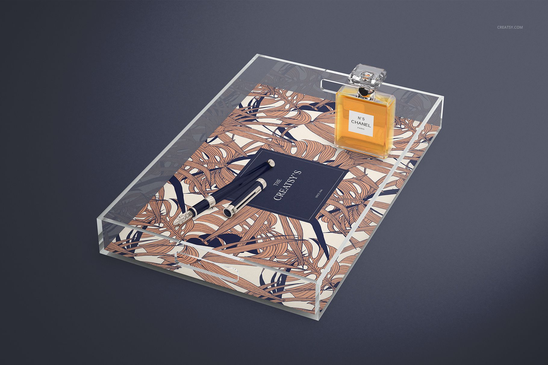 Clear lucite tray mockup featuring a decorative base, pen, notebook, and perfume bottle from an angled top view.