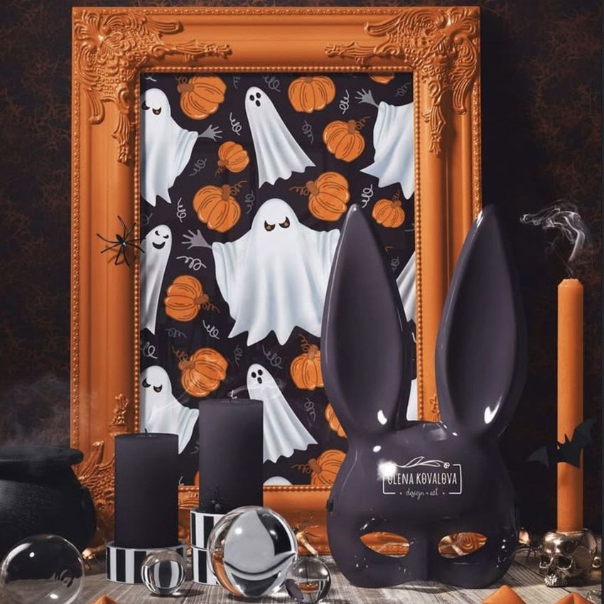 Halloween picture frame mockup featuring an ornate orange frame with ghost and pumpkin art, surrounded by candles and a black rabbit mask.