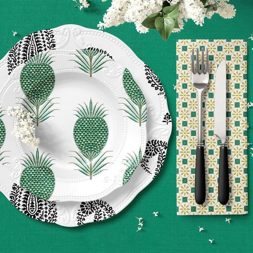 Placemat mockup featuring a white plate with green and black pineapple patterns, a patterned napkin, and cutlery on a green tablecloth.