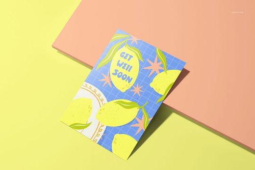 A5 card mockup with a colorful lemon pattern and 'Get Well Soon' text, shown from a top angle on a pastel surface.