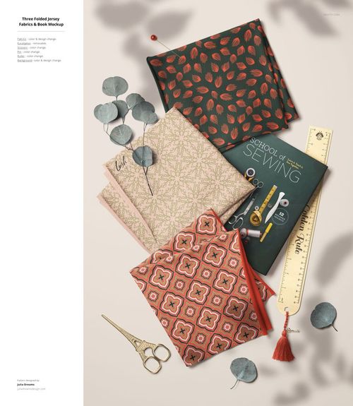 PSD mockup showing stacked jersey fabrics with intricate designs, eucalyptus leaves, and sewing accessories on a beige surface.