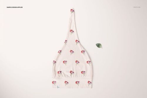 PSD mockup of a baby swaddle hat in a top view, decorated with small floral designs and placed beside a green leaf.