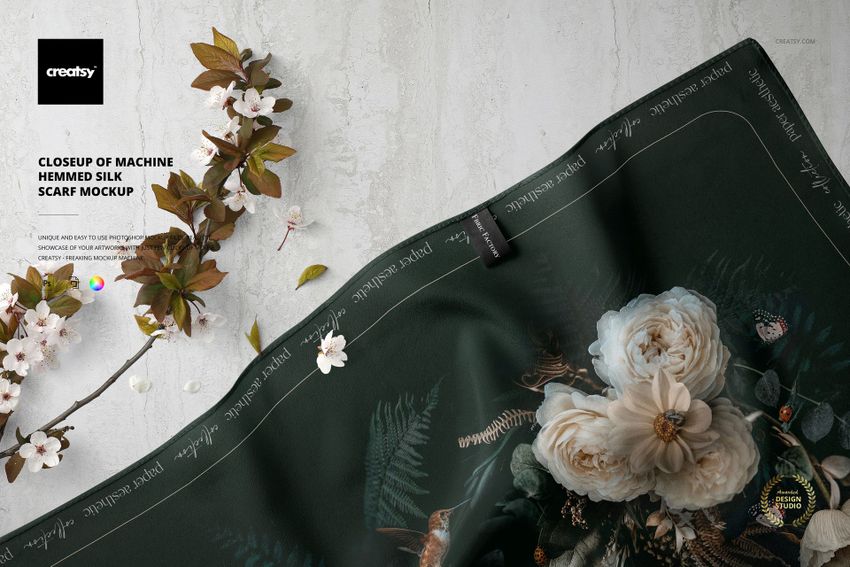 Silk scarf mockup shown from above, displaying detailed machine hemming and botanical designs on a green background.