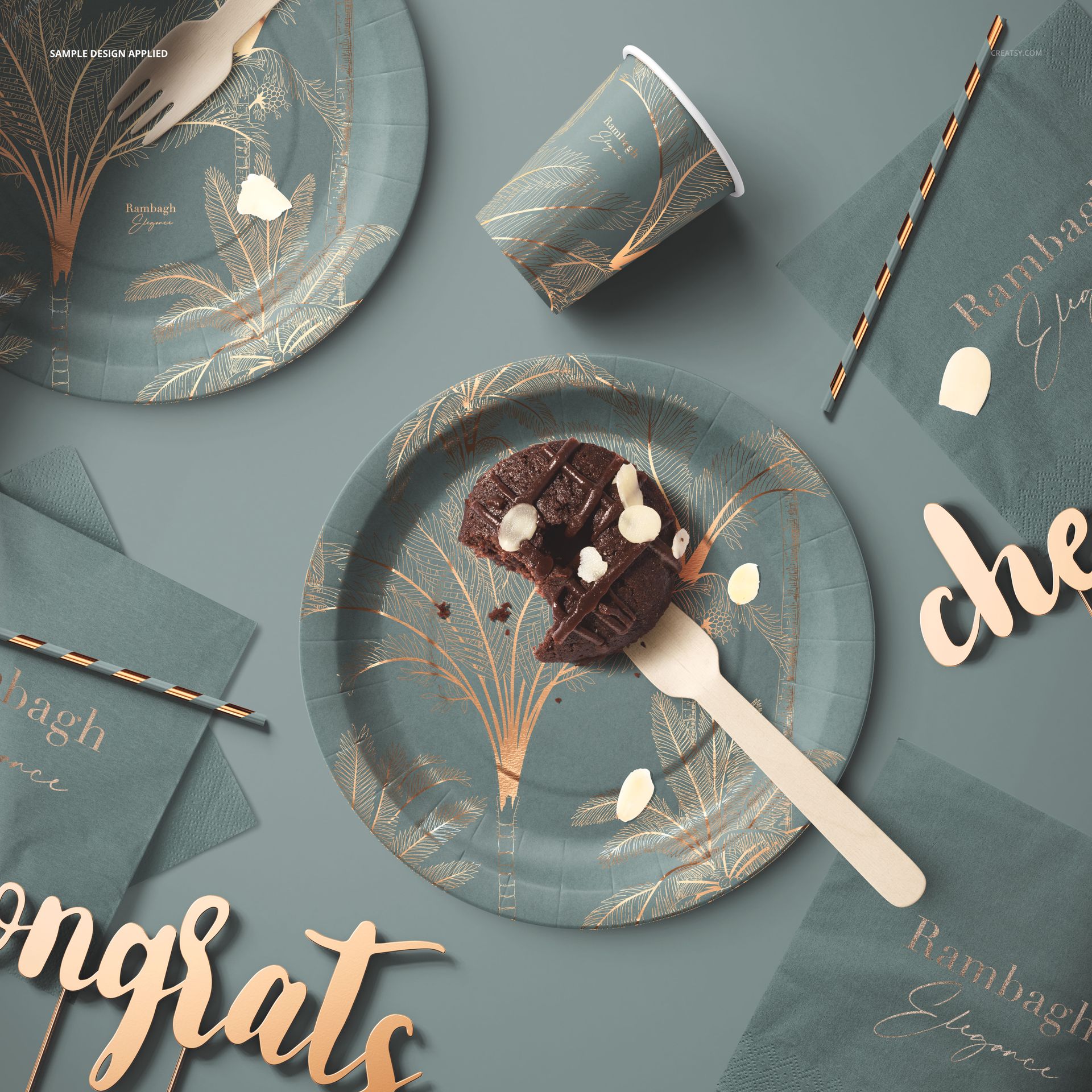 Party supplies mockup showing green paper tableware set with tropical gold designs, including plates, cups, napkins, and straws.