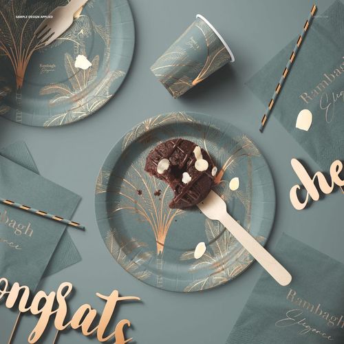 Party supplies mockup showing green paper tableware set with tropical gold designs, including plates, cups, napkins, and straws.