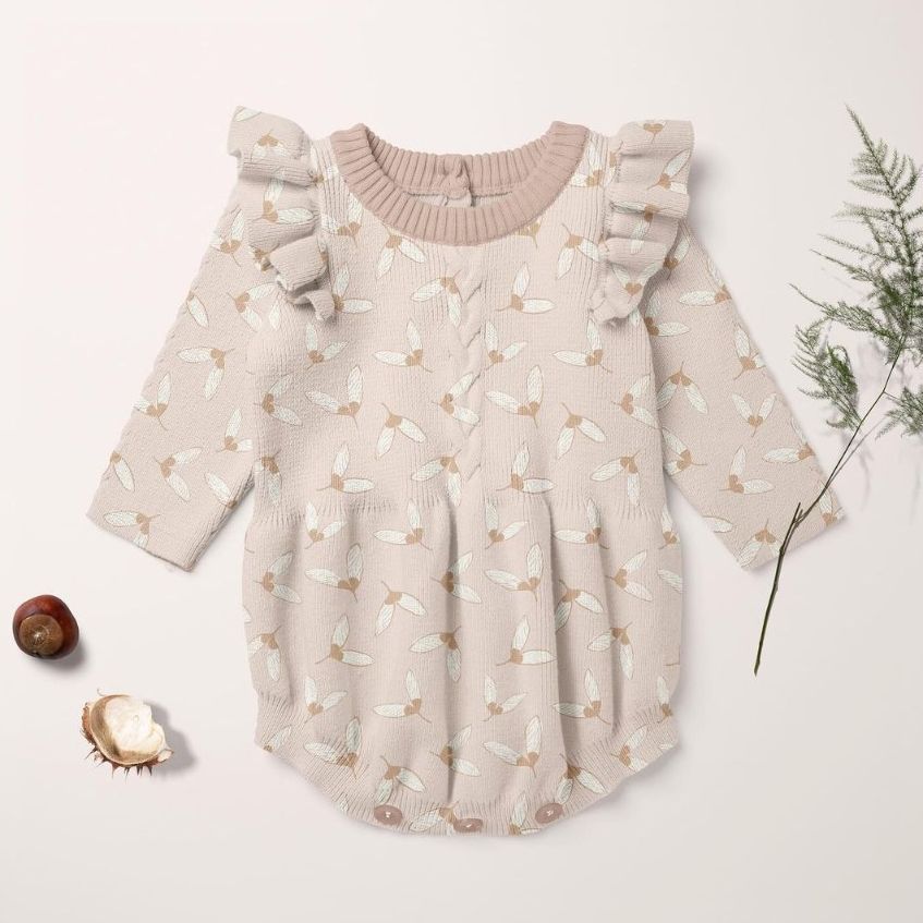 Knitted romper mockup featuring a long-sleeve baby outfit with ruffled shoulders and a light beige pattern, placed on a pale background.