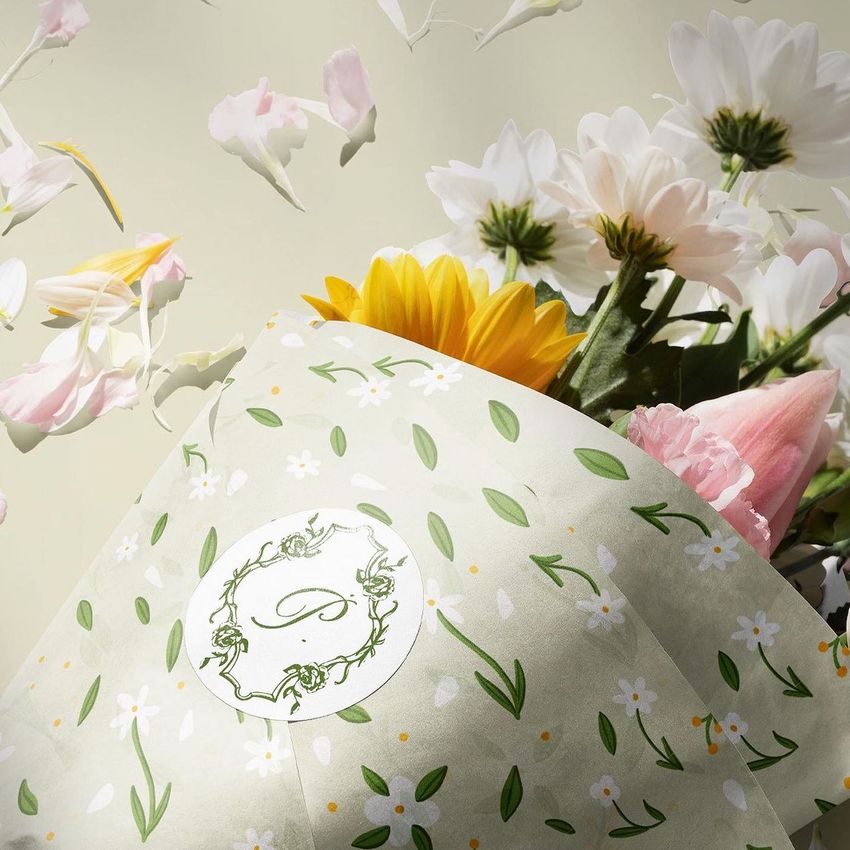 Flowers packaging mockup featuring a bouquet wrapped in light green paper with a floral pattern and a round label.