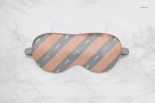 Adult eye mask mockup featuring alternating peach and gray stripes, displayed flat on a white marble surface.
