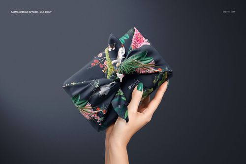 Furoshiki fabric wrap mockup featuring a dark silk cloth with botanical print, shown from the front in a hand.